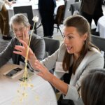 Photo taken during the Together25Ensemble conference featuring a woman constructing a tower out of straws